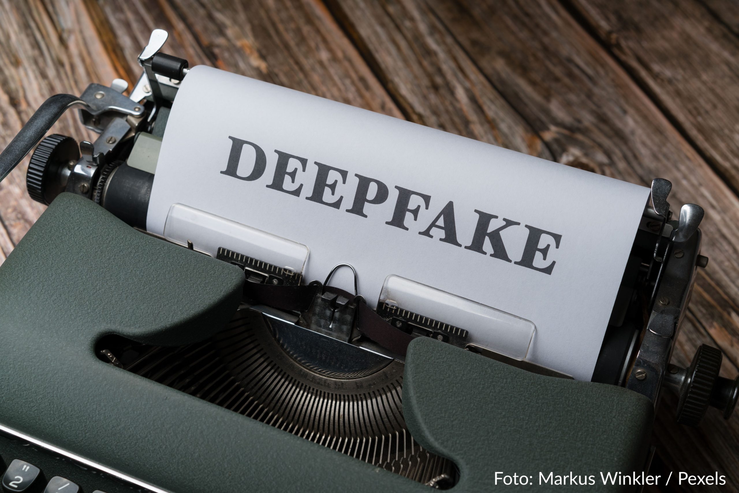 Auf dem Bild ist eine Schreibmaschine abgebildet, darin heftet ein Blatt Papier, auf dem fettgedruckt in Großbuchstaben das Wort Deepfake geschrieben steht.